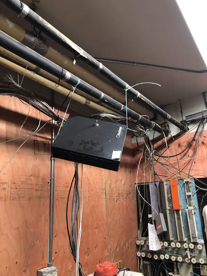An alarm cabinet hanging crookedly among loose wires and pipes